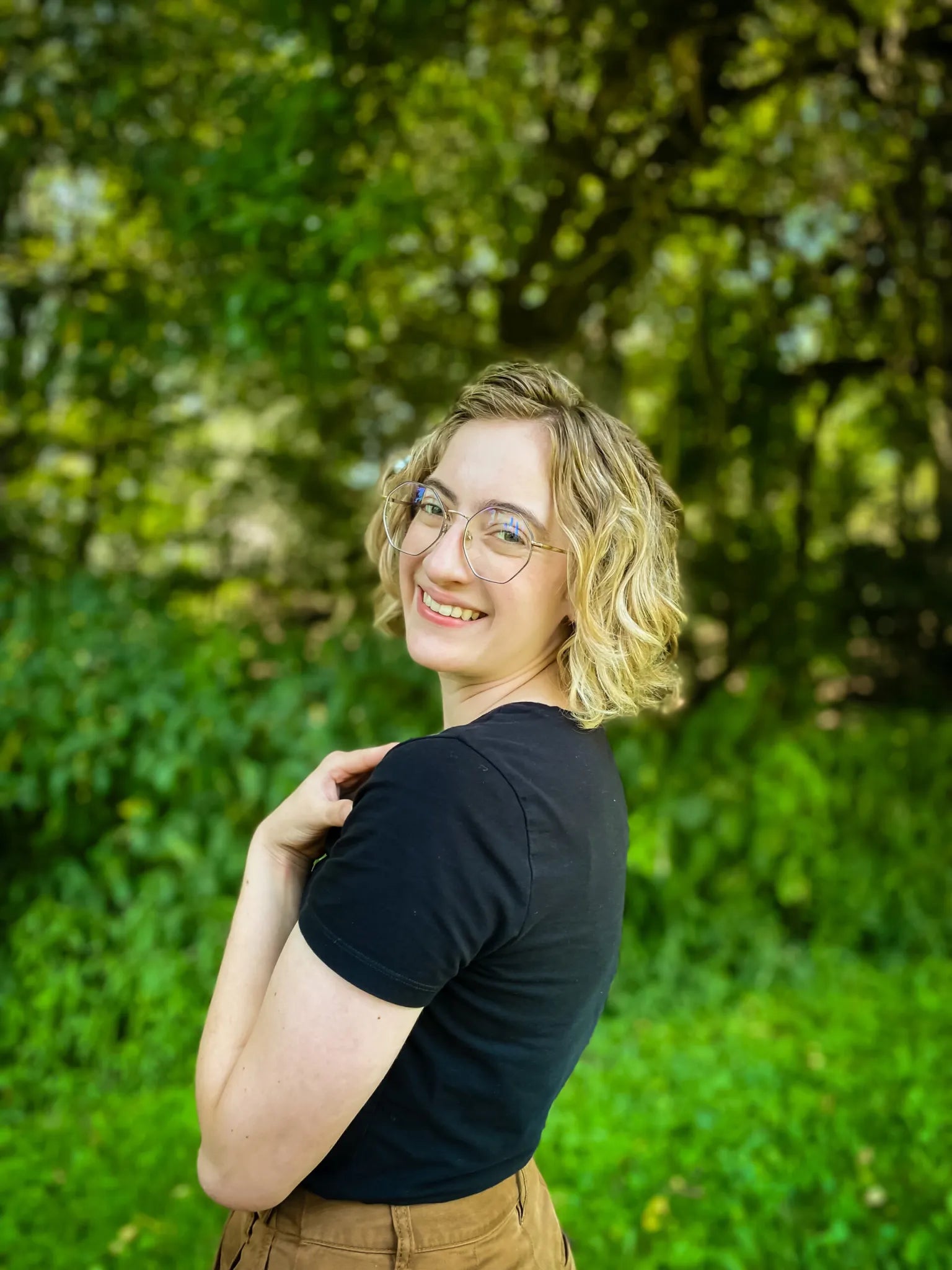 Lamplighter Literary Creations owner Megan standing in a green, leafy outdoor setting