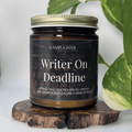 Candle jar labeled 'Writer On Deadline' on a wooden stand with a plant in the background