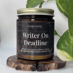 Candle jar labeled 'Writer On Deadline' on a wooden stand with a plant in the background